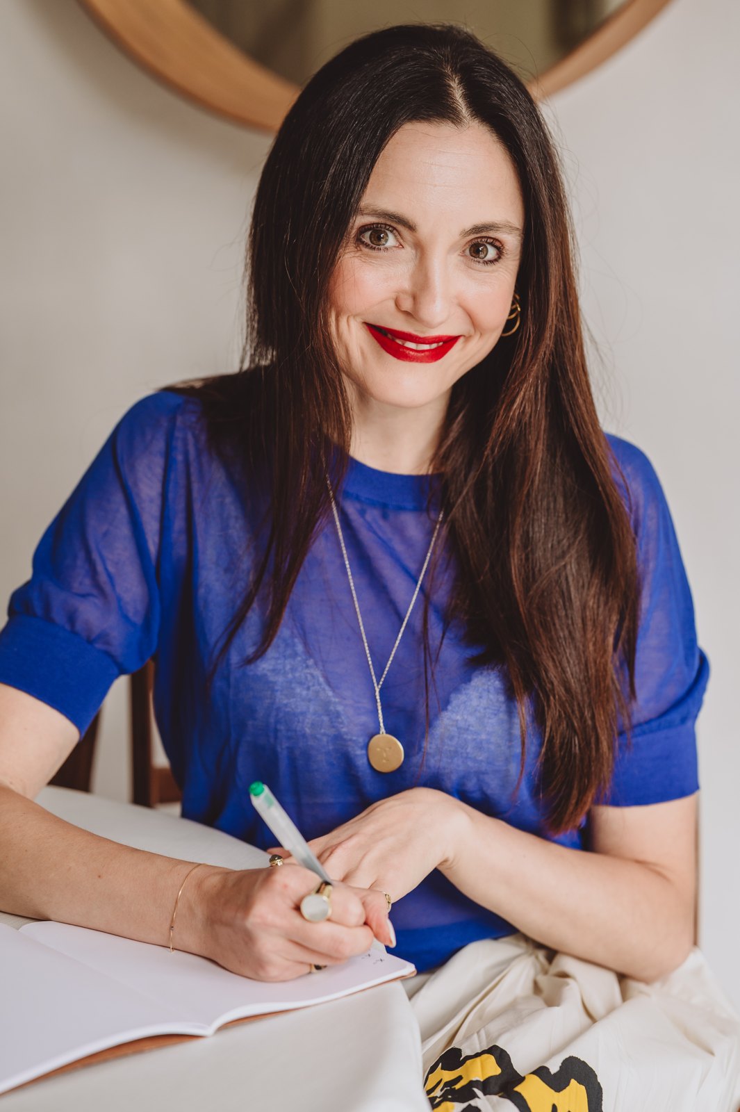 Nina Gigante sorride, con una maglia blu e una penna in mano, mentre scrive su un quaderno
